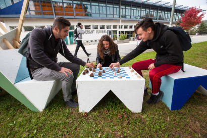 trois étudiants en train de jouer aux échecs sur du mobilier d'extérieur en carton.