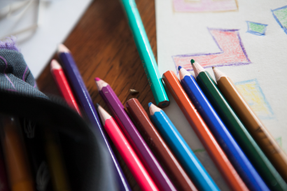 Des crayons de couleur posés sur un dessin d'enfant.