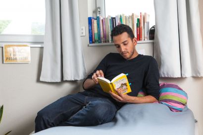 Un étudiant en train de lire un livre sur un lit.