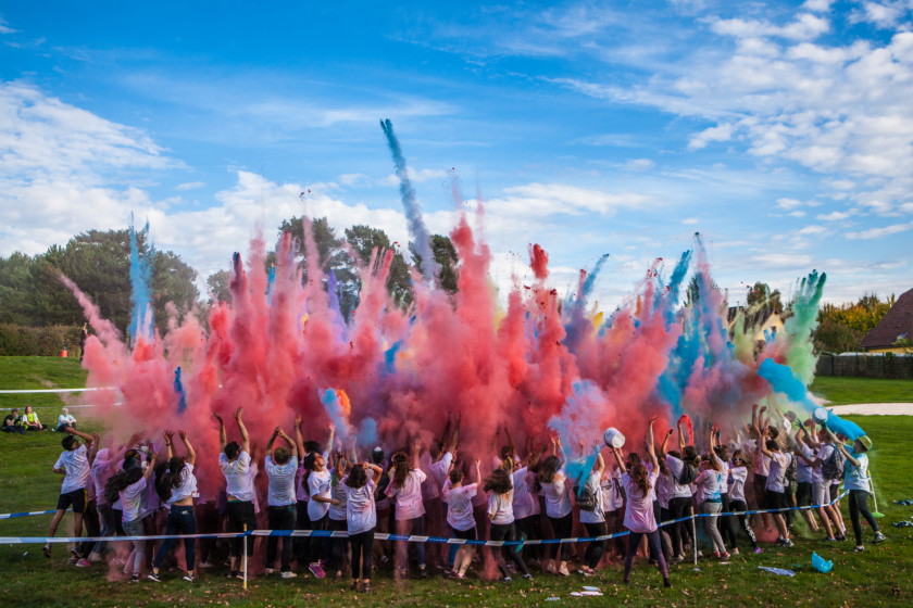 Un grand groupe d'étudiant au dessus duquel un gros nuage de poudre colorée évoque un feu d'artifices