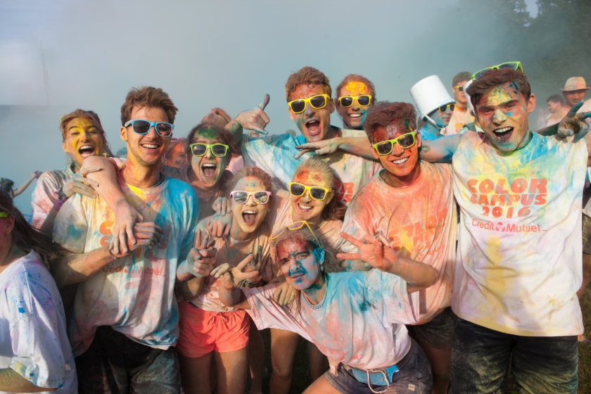 Des étudiants recouverts de poudre colorés en groupe font signe au photographe.