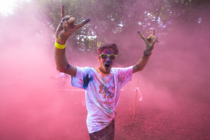 Un étudiant dans un nuage de poudre rose fait un signe victorieux au photographe.