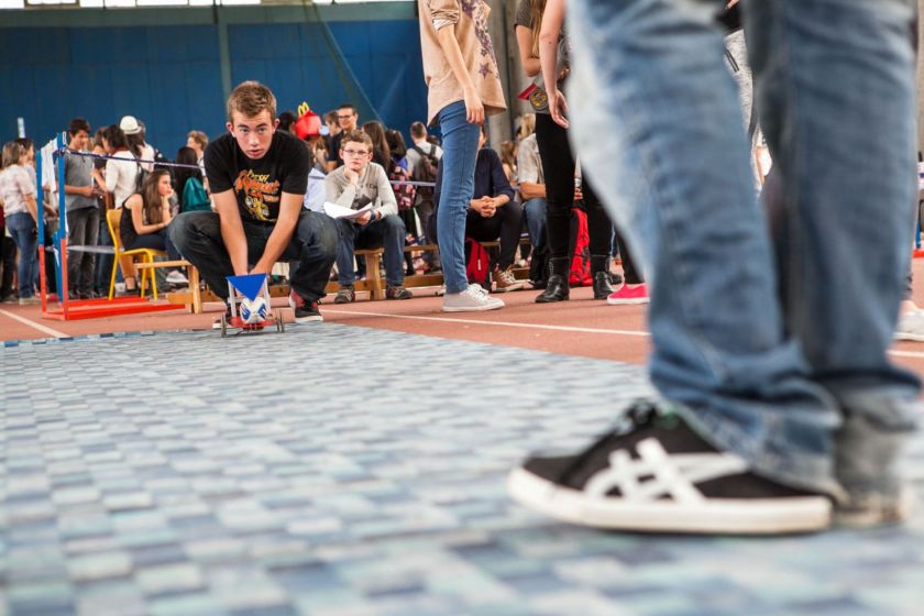 Un collégien accroupi s'apprête à lancer son robot sur la piste.