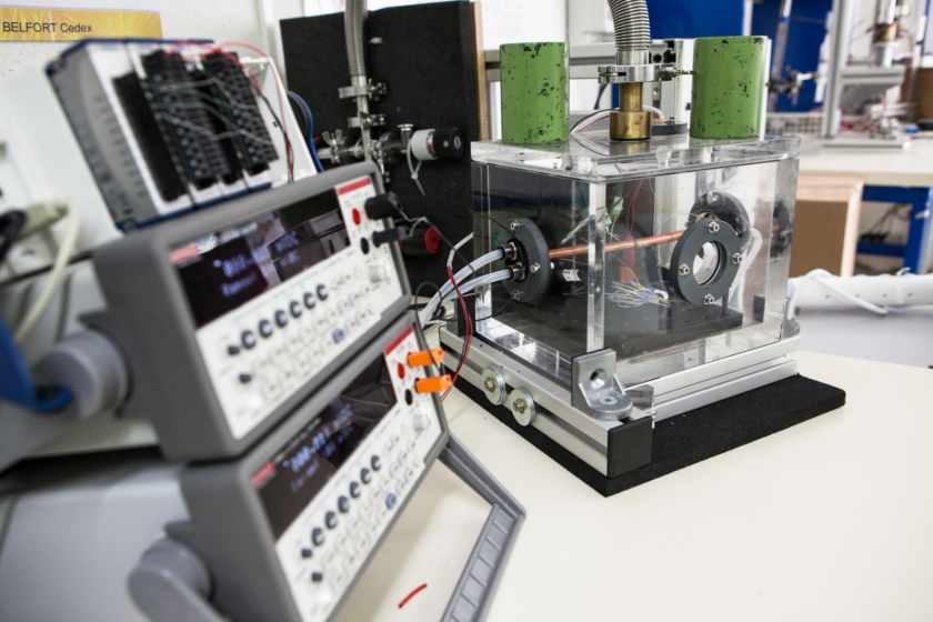 Un cube de plexiglass branché à divers tuyaux et à des appareils de type oscilloscope.