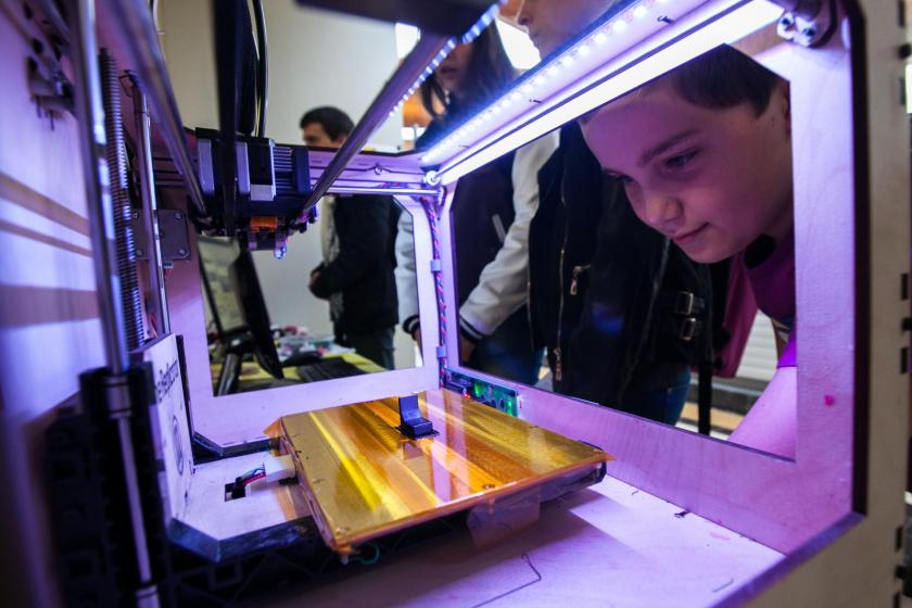Un jeune garçon regarde à l'intérieur d'une imprimante 3D