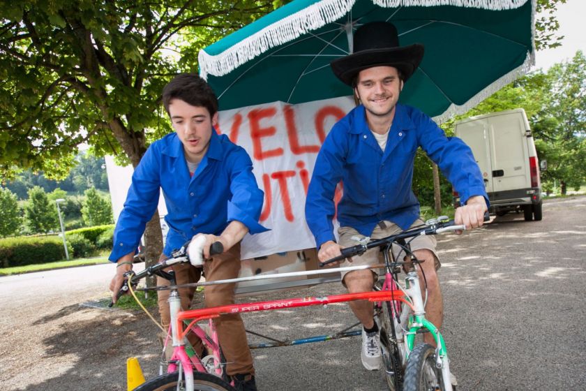 Deux jeunes hommes sur un double vélo équipés d'un parasol.