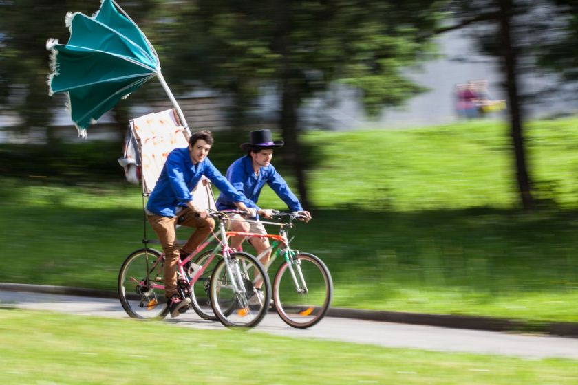 Deux jeunes hommes en veste bleue roulent sur un tandem parallèle équipé d'un parasol.