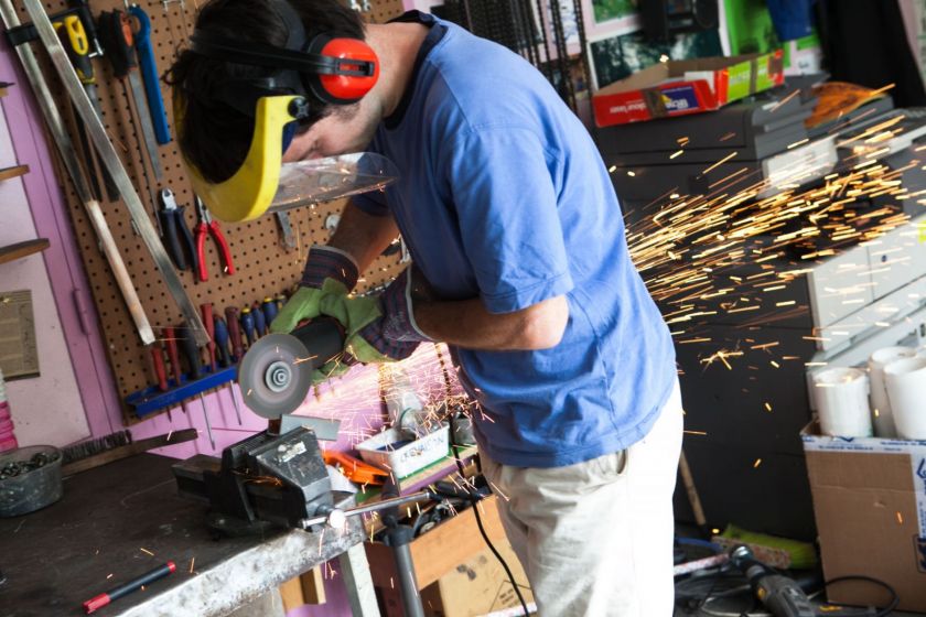 Un jeune homme dans un atelier avec un masque de protection et des gants en train d'utiliser une disqueuse qui fait des étincelles.