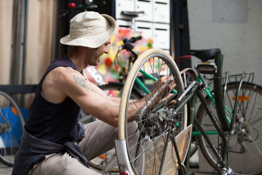 Un homme souriant, accroupi, en train de bricoler un vélo.