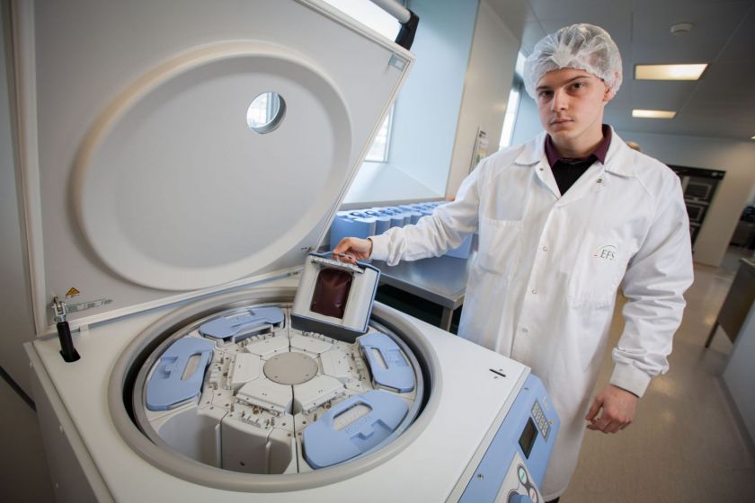 Floriant Paupert, en blouse et charlotte, s'apprête à placer une poche de sang dans une centrifugeuse.