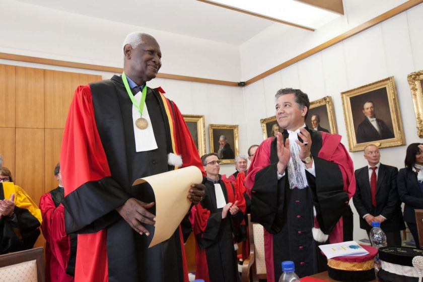 Abdou Diouf, en toge, tient un diplôme. Jacques Bahi applaudit. Derrière, un certain nombre de personnes en toge applaudissent également.