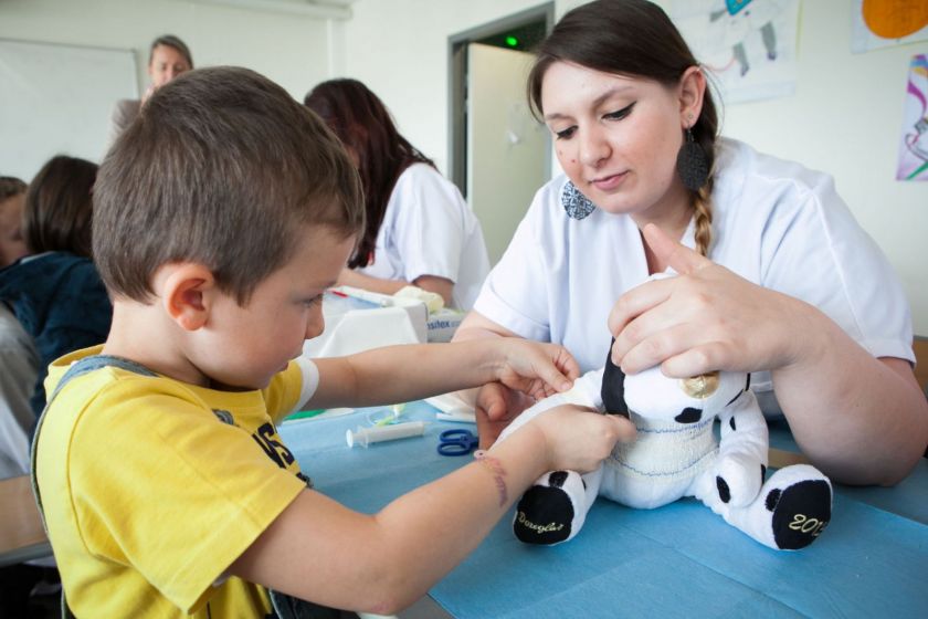 Un petit garçon termine un bandage sur son nounours aidé par une étudiante infirmière.