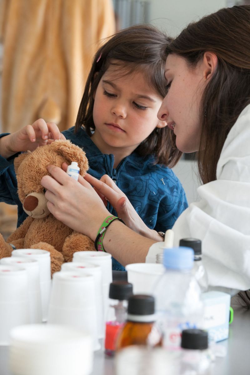 Une petite fille examine les oreilles de son nounours malade en compagnie d'une étudiante en pharmacie.