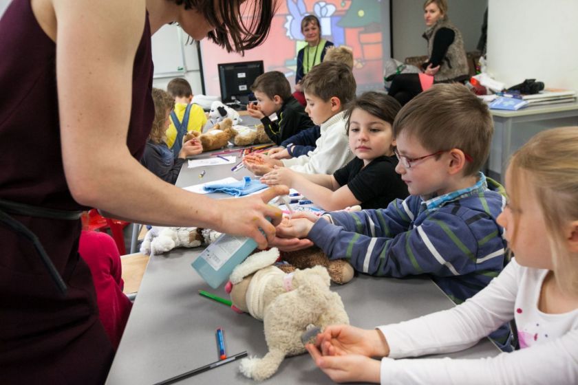 Une jeune femme donne du savon à une série d'enfants assis qui tendent les mains.