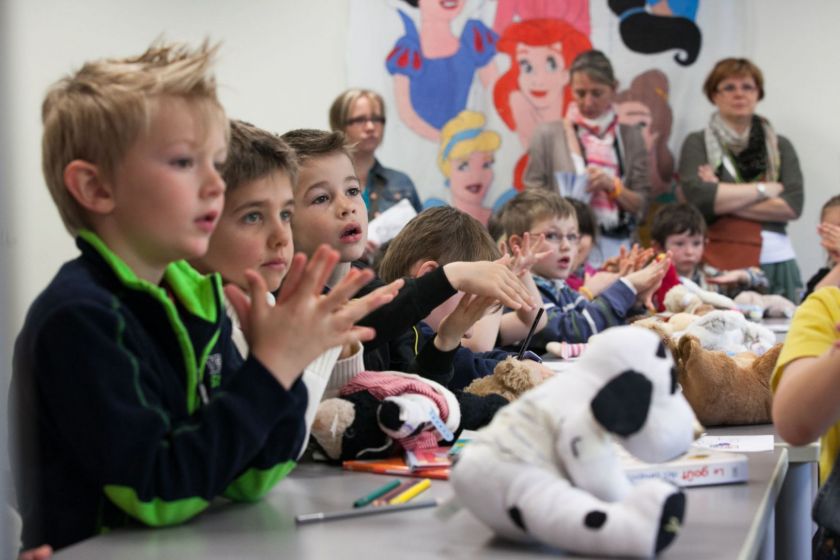 Plusieurs enfants assis à table et attentifs se frottent les mains.