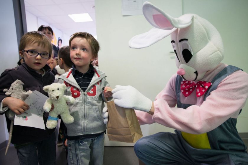 Un homme déguisé en lapin tend un sac en papier à un enfant. Une série d'enfants sont placés en rang.