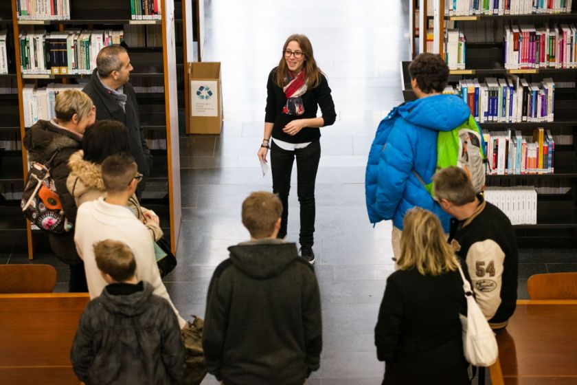 Une étudiante face à un groupe de visiteurs dans une bibliothèque.