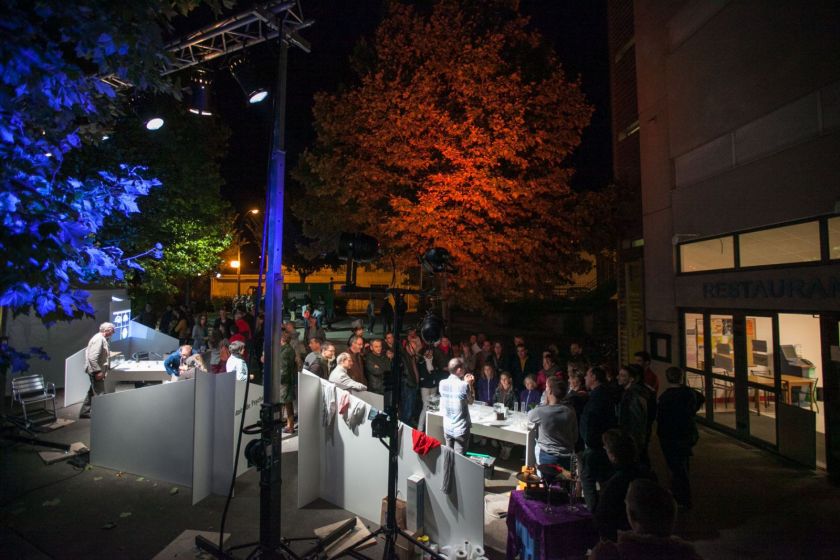 Une foule de visiteurs rassemblé devant des stands. Eclairages colorés dans les arbres.