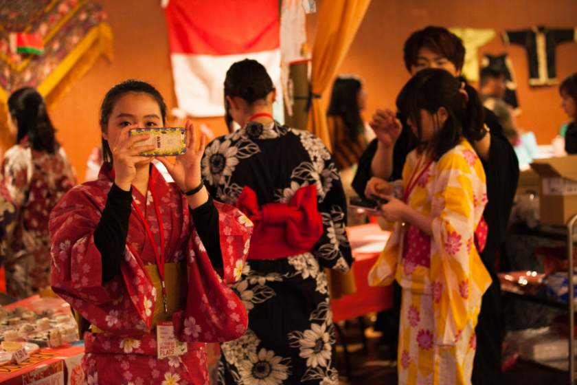 Plusieurs jeunes japonais en kimono. Une jeune fille prend une photo avec son téléphone portable. Un jeune homme ajuste la coiffure d'une autre.