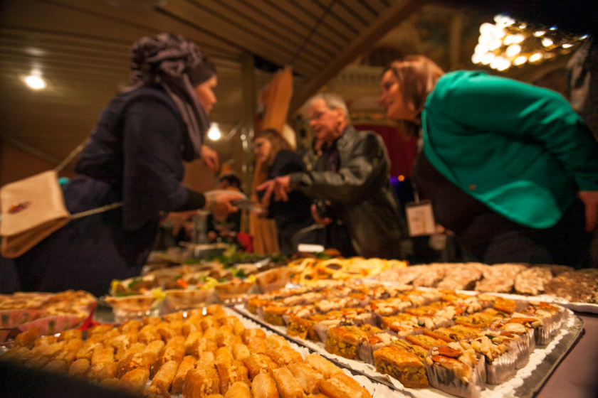 Une table pleine de pâtisseries orientales avec des personnes floues en arrière-plan.