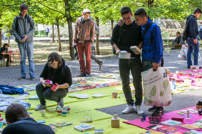 Image de brocante : des jeunes gens en train d'inspecter des objets disposés par terre sur des nappes.