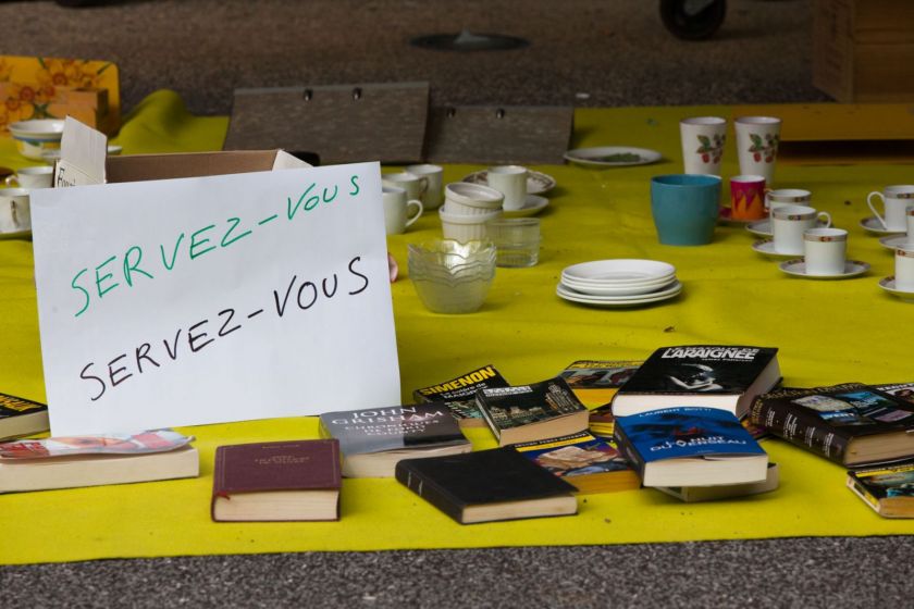 Des affaires (livres, vaisselle) posés au sol avec un écriteau "servez-vous"