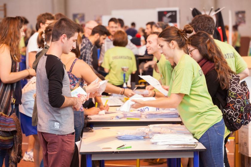 Un stand avec du monde et une jeune fille qui donne un tee-shirt à un étudiant.