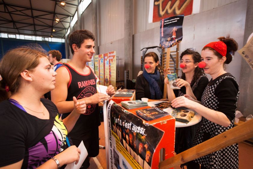 Plusieurs jeunes femmes portant un nez rouge de clown en train de discuter avec des étudiants sur un stand.