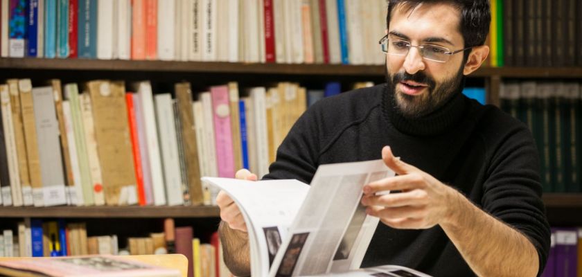 Anton Alvar Nuno feuillette un livre. Une bibliothèque en fond.