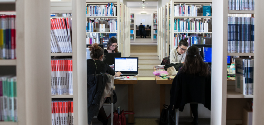 Vue intérieure de la BU Santé avec des rayonnages de livres et des étudiantes qui travaillent sur des ordinateurs.