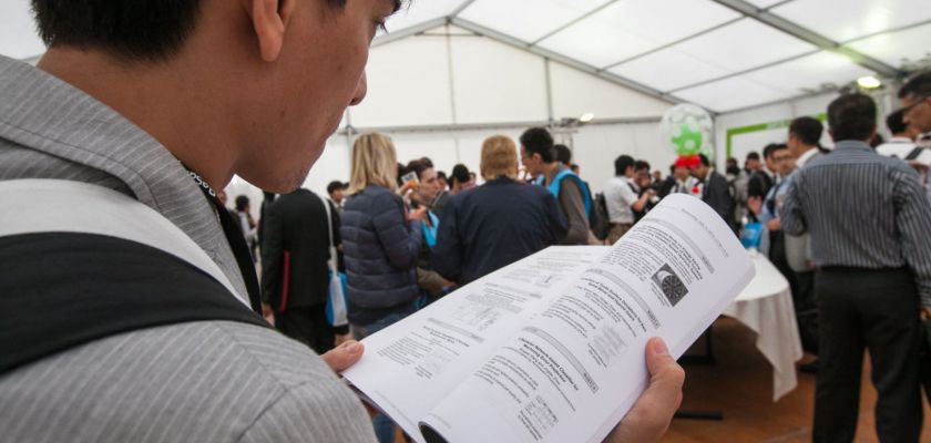 Un homme asiatique de dos feuillette un document scientifique. Beaucoup de monde debout en arrière-plan.