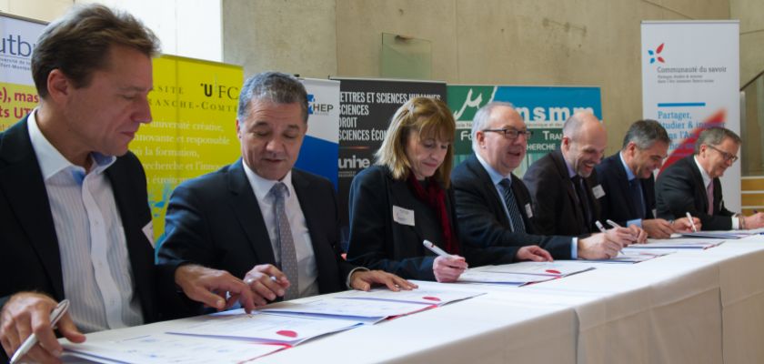 Une série de 7 directeurs d'établissements d'enseignement supérieur assis à une table pour la signature d'une convention.