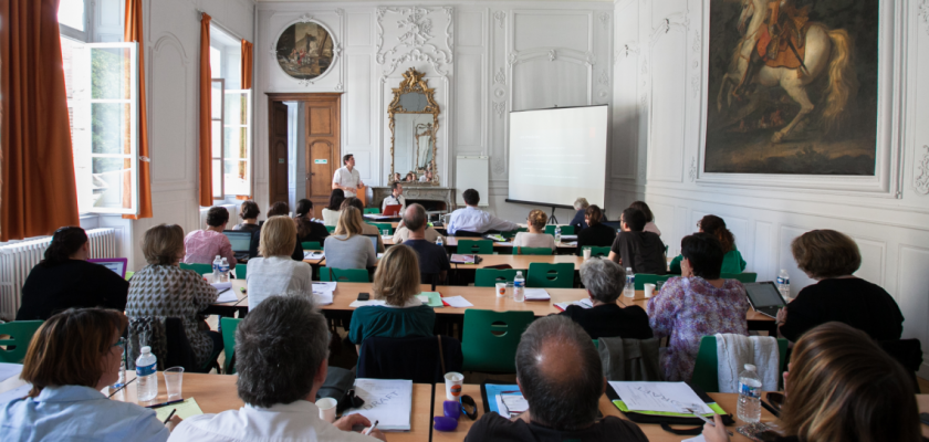 Grand salon de l'UFR SLHS : un homme fait une présentation devant la salle pleine. Au mur un tableau représentant Louis XIV sur un cheval.