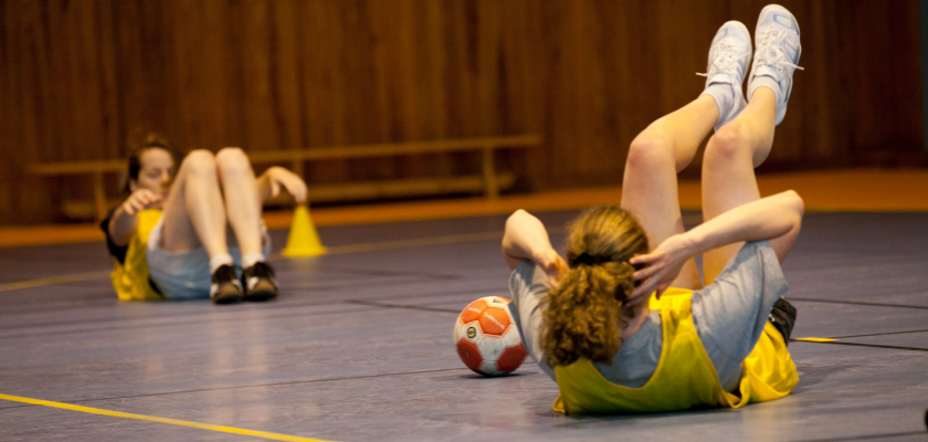 Deux jeunes filles en tenue de hanball en train de faire des exercices sportifs au sol