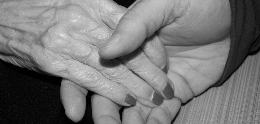 Une main maigre de personne âgée tenue par une autre main