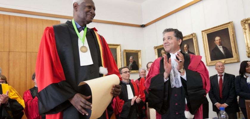 Abdou Diouf, en toge, tient un diplôme. Jacques Bahi applaudit. Derrière, un certain nombre de personnes en toge applaudissent également.