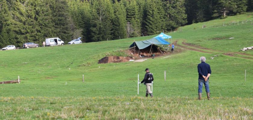 Deux hommes de dos devant un chantier de fouilles en extérieur.