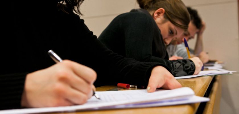 Des étudiants en train d'écrire sur des copies dans un amphithéâtre.