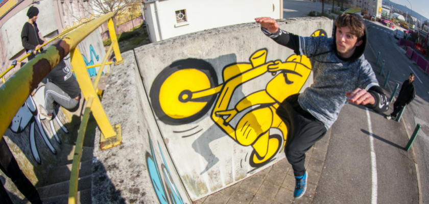 Un jeune homme suspendu dans les airs à côté d'un mur dans un décor urbain.