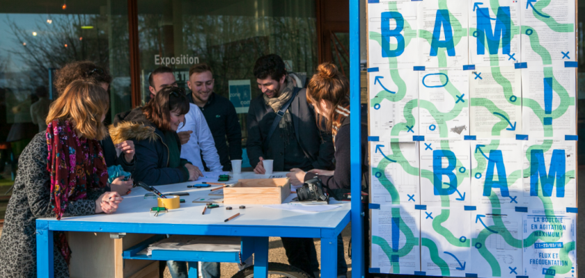 Un atelier mobile avec des affiches indiquant BAM et différentes personnes souriantes autour d'un plan de travail.