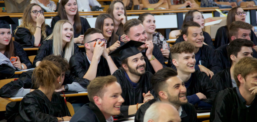 Des étudiants souriants en toge et toques de diplômés dans un amphithéâtre