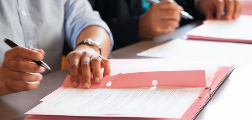 Des mains qui tiennent un stylo, en train de signer un document sur un parapheur.