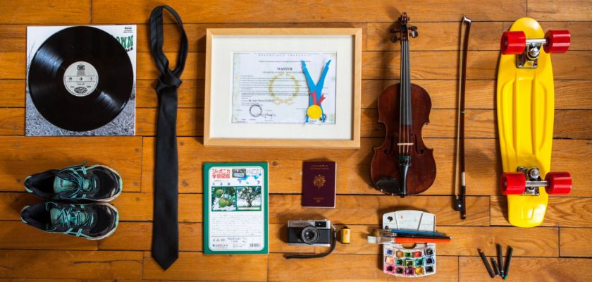 Plusieurs objets (violon, chaussures de sport, passeport, cravate, skate-board, pinceaux et peinture, appareil photo...) encadrent un diplôme.