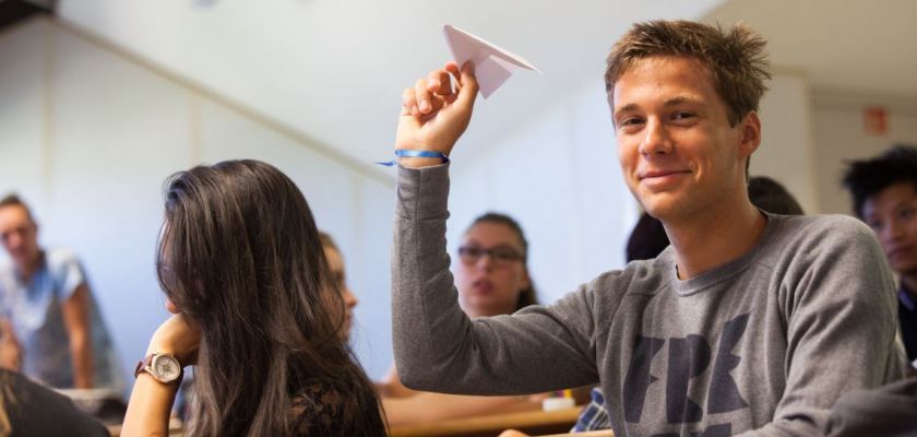 Un étudiant brandit un avion en papier.