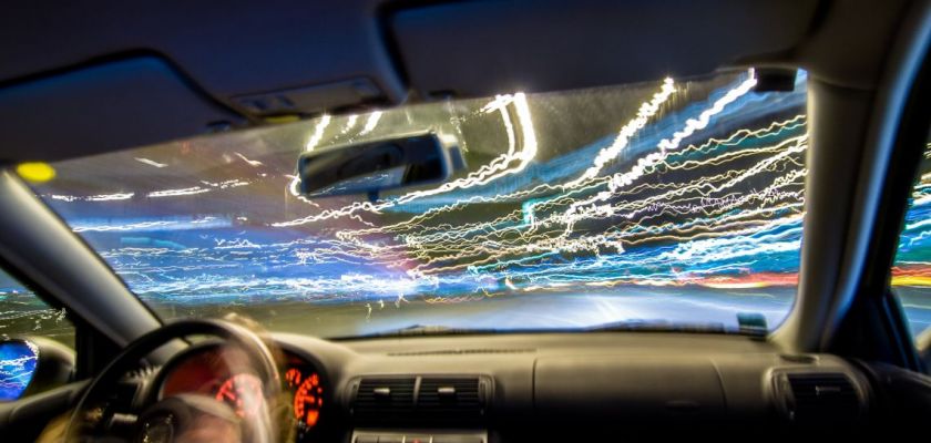 Un pare-brise de voiture vu de l'intérieur avec des lignes lumineuses colorées sur la route.