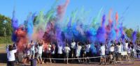Un groupe de jeunes gens en tee shirt blanc de dos. Au dessus d'eux, une explosion de poudre colorée.