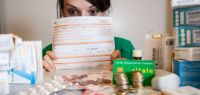 Une jeune femme derrière une feuille de soins regarde une pile de médicaments et d'argent.