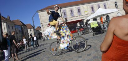 Place de la révolution à Besançon : un jeune homme perché sur un vélo très haut fait signe au photographe.