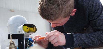 Un jeune garçon répare un robot à l'aide d'un tournevis.