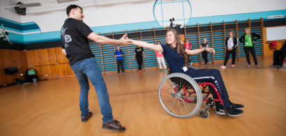 Une jeune fille dans un fauteuil roulant danse avec un homme debout. Ils se tiennet par la main.